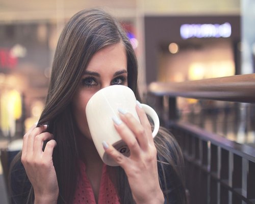 Woman drinking morning tea by a large window overlooking the city